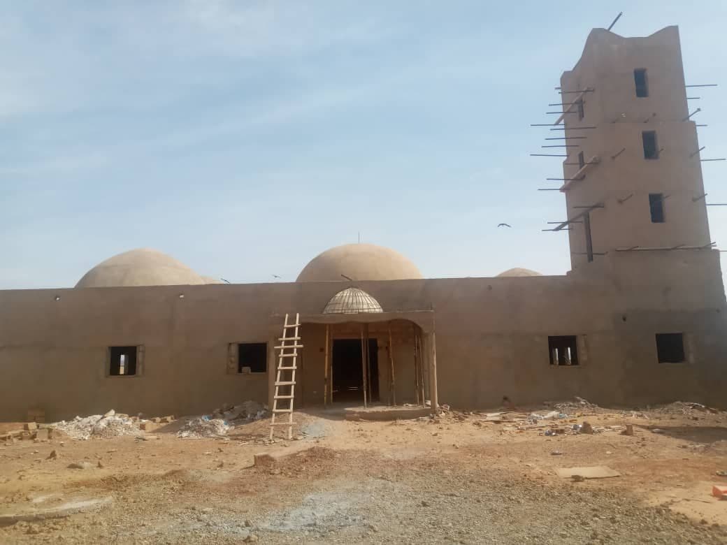 Mosquée achevée : coupoles blanches, minaret et mur d'enceinte